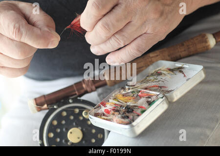 Ein Fischer mit Fliege Angelrute und Kunstköder-Box hält eine rote Fliege. Stockfoto