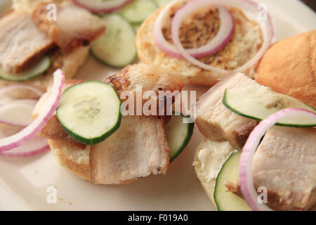 Schweinebauch, geröstet und auf kleine Brötchen mit Gurke und Zwiebel in Scheiben geschnitten Stockfoto