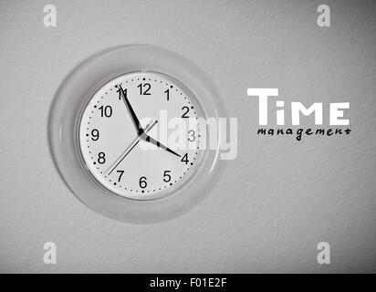 Uhr an der Wand mit "Zeitmanagement"-Schriftzug, schwarz / weiß Foto Stockfoto