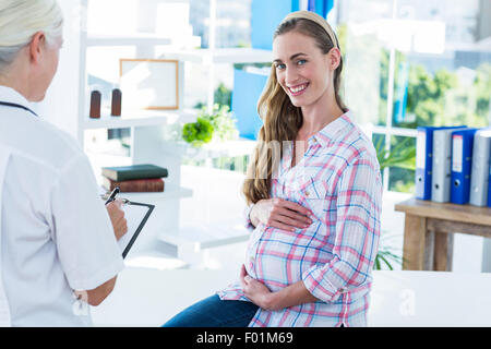 Schwangere Frau lächelt in die Kamera auf einem Untersuchungstisch Stockfoto