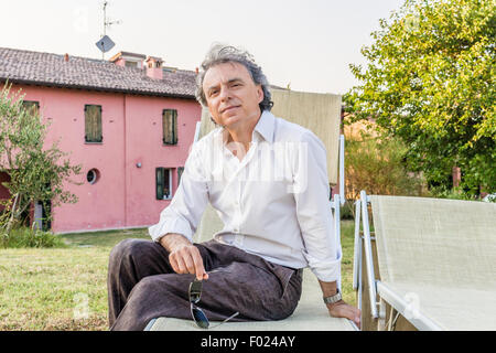 faszinierende wohlhabenden Gentleman von vierzig aus Stadt ruht auf einem Liegestuhl im Garten von einem roten Landhaus in Italien Stockfoto