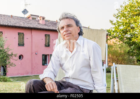 faszinierende wohlhabenden Gentleman von vierzig aus Stadt ruht auf einem Liegestuhl im Garten von einem roten Landhaus in Italien Stockfoto