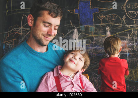 Kleiner Junge mit Junge im Hintergrund auf Vaters Schoß sitzen Stockfoto