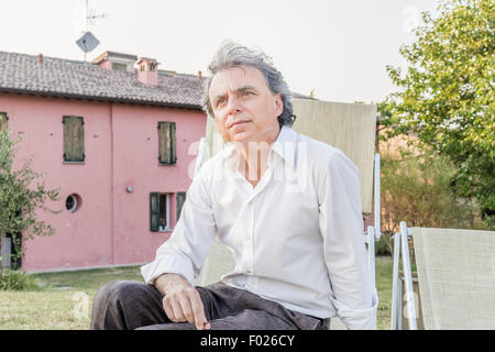 faszinierende wohlhabenden Gentleman von vierzig aus Stadt ruht auf einem Liegestuhl im Garten von einem roten Landhaus in Italien Stockfoto