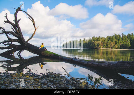 Bildnis eines Knaben sitzen auf einem umgestürzten Baum im See Stockfoto