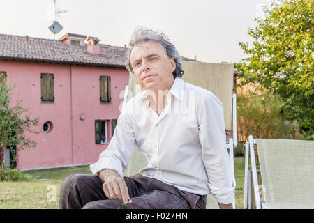 faszinierende wohlhabenden Gentleman von vierzig aus Stadt ruht auf einem Liegestuhl im Garten von einem roten Landhaus in Italien Stockfoto