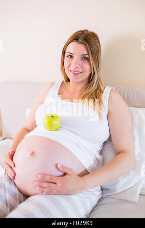 Schwangere Frau auf Bett liegend mit Apfel im Bauch Stockfoto