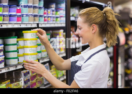 Lächelnde blonde Arbeiter unter einem Produkte im Regal Stockfoto