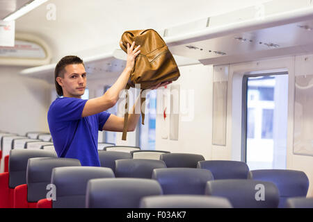 Junger Mann, der Gepäck ins Gepäckfach am Zug Stockfoto