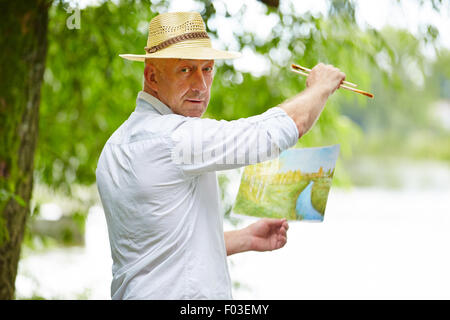 Senior Malerei Künstler mit Bild in der Natur im Sommer Stockfoto