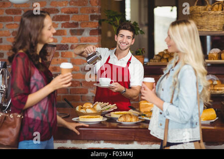 Lächelnden Kellner gießt Milch in einer Tasse Kaffee Stockfoto