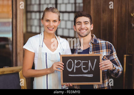 Lächelnde Kellnerin und Mann hält Tafel mit Schild "geöffnet" Stockfoto