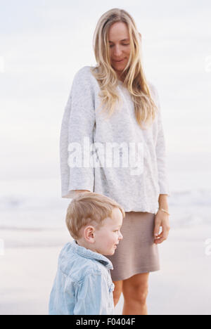 Lächelnde Frau, stehend auf einem Sandstrand am Meer mit ihrem kleinen Sohn. Stockfoto