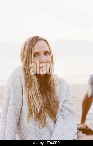 Frau sitzt auf einem sandigen Strand in einen Jumper am Ende des Tages. Stockfoto