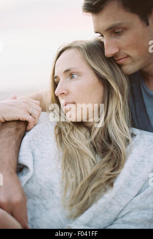 Ein paar, Mann und Frau sitzen auf einem Strand Arme umeinander, in der Dämmerung. Stockfoto