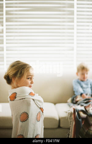 Junges Mädchen, eingewickelt in ein Handtuch und ein kleiner Junge auf einem Sofa sitzt. Stockfoto