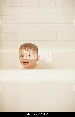 Kleiner Junge sitzt in der Badewanne Baden, lächelnd in die Kamera. Stockfoto