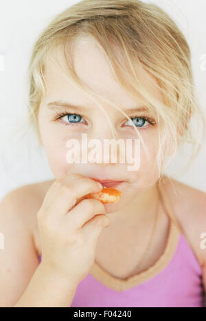 Porträt eines jungen blonden Mädchens, Essen eine Mandarine in die Kamera schaut. Stockfoto