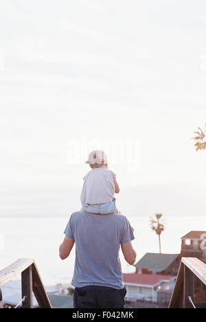 Rückansicht eines Mannes, der seine kleine Tochter auf seinen Schultern tragen. Stockfoto