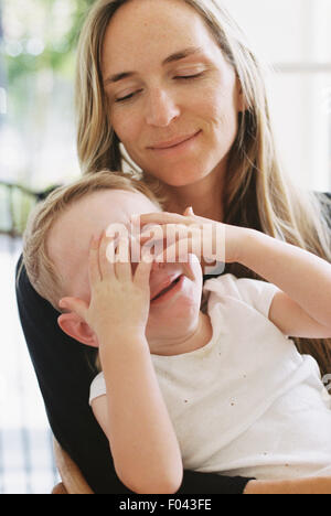 Ein Junge sitzt auf seinem Schoß Mütter mit seinen Händen über die Augen. Stockfoto