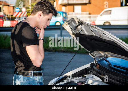 Hübscher junger Mann versucht, einen Automotor, reparieren Blick in offene Motorhaube Stockfoto