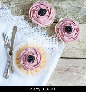 Ansicht von oben drei Blackberry Cupcakes auf rustikalen Holztisch mit geschnürten Tischdecke und Vintage Besteck Stockfoto