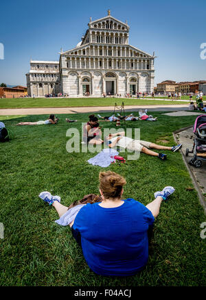 Touristen, die auf dem Gras im Schatten sitzen und den Blick auf die Kathedrale von Pisa genießen. Italien Stockfoto