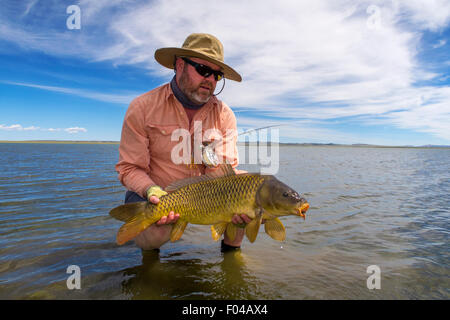 Fliegenfischer mit Karpfen gefangen in seichten See Stockfoto