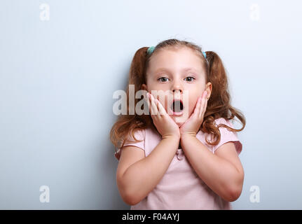 Spaß überraschend junge Mädchen mit geöffneten Mund auf blauem Hintergrund mit leeren Textfreiraum suchen Stockfoto