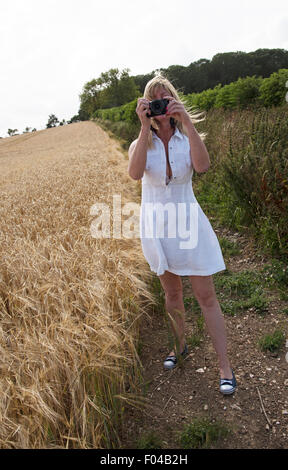 Frau mit einer Digitalkamera um zu fotografieren, ein Feld von Gerste in Hampshire Landschaft südlichen England Großbritannien Stockfoto