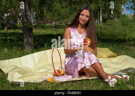 Glückliches Brünette Mädchen mit Apfel sitzt unter der Sonne im park Stockfoto