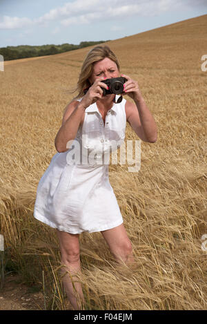 Frau mit einer Digitalkamera um zu fotografieren, ein Feld von Gerste in Hampshire Landschaft südlichen England Großbritannien Stockfoto