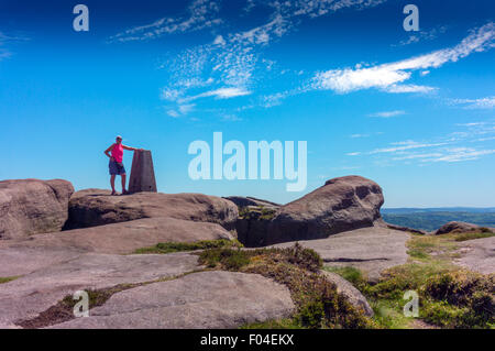 Einsame Figur an Trig, Triangulation Punkt oben Stanage Edge, Peak District National Park, Derbyshire, England, UK. Blauer Himmel Stockfoto