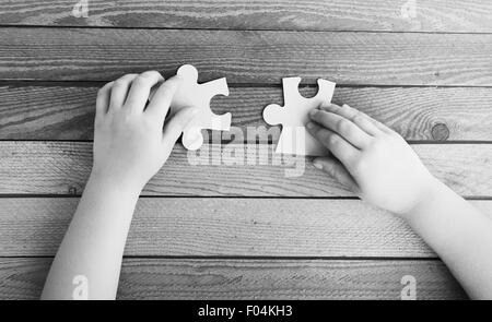 Bild Hände verbinden zwei Puzzleteile auf Holztisch, schwarz / weiß Foto abgeschnitten Stockfoto