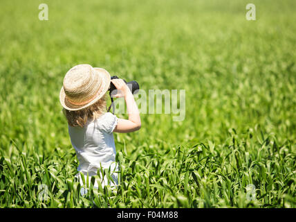 Kleine blonde Mädchen in Strohhut Blick durch ein Fernglas outdoor Stockfoto