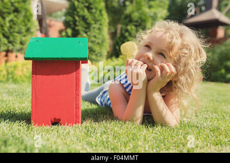 Kleine blonde Mädchen auf der Wiese liegend mit Haus Spielzeug Stockfoto