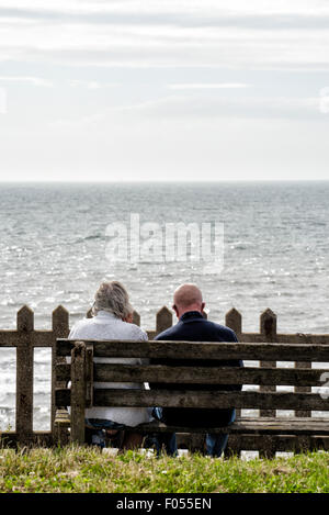 Ältere Paare sitzen auf Holzbank mit Blick aufs Meer. Stockfoto