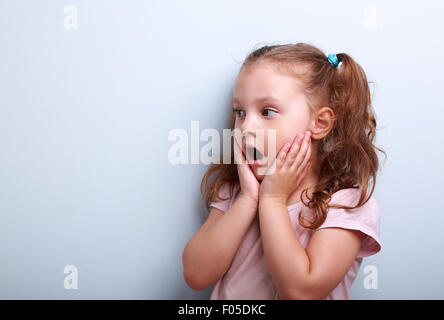 Überraschend junge Mädchen mit geöffneten Mund und Hand in der Nähe von Gesicht auf blaue Kopie Raum Hintergrund Stockfoto