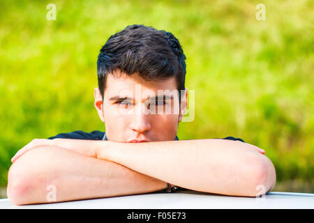 Kopf und arme Schuss von hübscher attraktiver junger Mann, Blick in die Kamera im Freien, stützte sich auf flache Oberfläche mit Kopf auf Seite Stockfoto