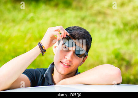 Kopf und arme Schuss von hübscher attraktiver junger Mann, Blick in die Kamera im Freien, stützte sich auf flache Oberfläche mit Kopf auf Seite Stockfoto