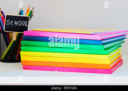 Multi farbige Bücher im Stapel auf dem hellen Bücherregal und Stifte in einem Fall vor dem Hintergrund Stockfoto