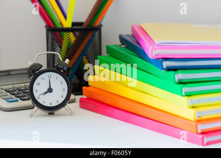 Konzept der Bildung. Schwarze Wecker. Multi farbige Bücher im Stapel auf den hellen Bücherregal, Taschenrechner und Stifte in Stockfoto