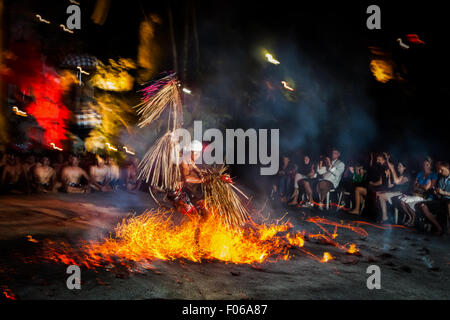 Ein Feuertanz-Darsteller läuft über einen Haufen brennender Kokosnüsse vor Touristen, während der Kecak- und Feuertanz-Show in Ubud, Gianyar, Bali, Indonesien. Stockfoto