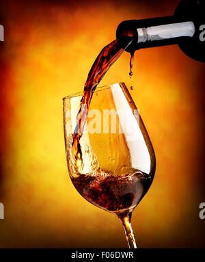 Rotwein in einem Weinglas auf orangem Hintergrund gießen Stockfoto