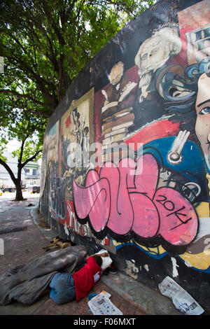 Nicht erkennbare armer Mann schlafen auf der Straße der Innenstadt von Caracas mit einem Graffiti von Simon Bolivar im Hintergrund. Stockfoto
