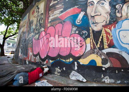 Nicht erkennbare armer Mann schlafen auf der Straße der Innenstadt von Caracas mit einem Graffiti von Simon Bolivar im Hintergrund. Die pover Stockfoto