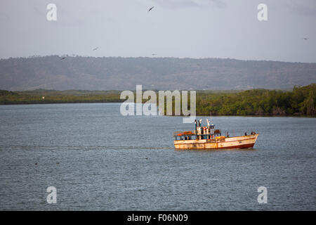 Alte verrostete Fischerboot auf dem Weg zum Hafen von Tucacas mit Abendlicht und Vögel in der Luft herumfliegen. Stockfoto