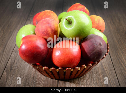 frische Pfirsiche und Äpfel im Korb auf Holztisch Stockfoto