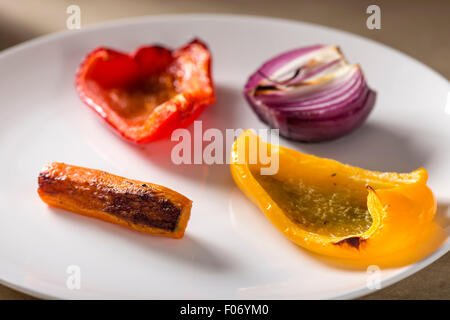 Gebratenes Gemüse auf eine weiße Servierplatte. Karotte, rote Zwiebeln, rote und gelbe Paprikaschote Stockfoto