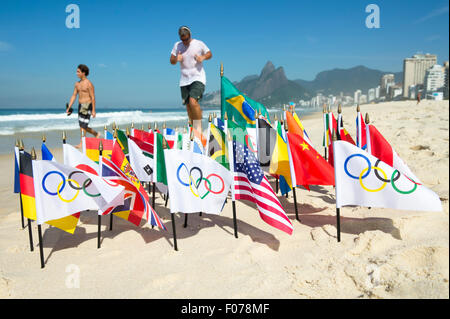 RIO DE JANEIRO, Brasilien - 20. März 2015: Menschen passieren eine Gruppe von Olympische Fahnen sowie eine Reihe anderer im Sand. Stockfoto